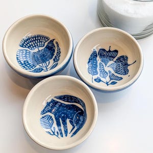 Può includere: Tre piccole ciotole in ceramica bianca con disegni blu e bianchi. Le ciotole presentano un uccello, foglie e una volpe.