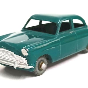 May include: A teal-coloured vintage toy car with a silver grille and headlights. The classic car has a two-door design and sits on four small wheels. The paint shows signs of wear, adding to its antique charm.