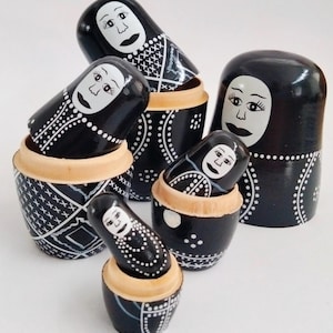 Peut inclure: Ensemble de poupées russes noires, ornées de visages blancs et de motifs décoratifs. Les poupées, partiellement emboîtées, présentent des motifs traditionnels, un exemple de l'art populaire russe.