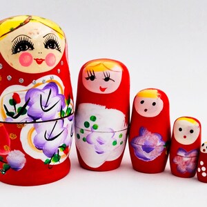 Peut inclure: Ensemble de cinq poupées russes, ou Matriochkas, de tailles décroissantes. Les poupées sont peintes en rouge avec des motifs floraux et des visages. La plus grande poupée mesure environ 15 cm de haut.