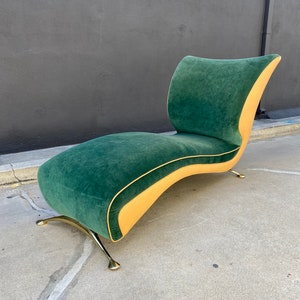 May include: A mid-century modern chaise lounge with a curved design. The seat and back are upholstered in a deep green velvet fabric, with a contrasting tan border. The legs are made of gold-toned metal.