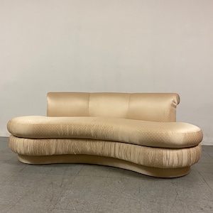 May include: A curved, cream-colored sofa with a rounded back and a low, curved base. The sofa is upholstered in a fabric with a subtle polka-dot pattern. The design is reminiscent of mid-century modern furniture.