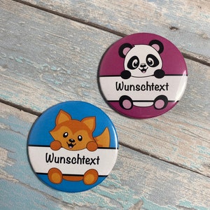 Könnte beinhalten: Zwei runde, bunte Knöpfe mit Comic-Tieren. Der erste Knopf ist blau mit einem Fuchs, der über einem weißen Banner mit der Aufschrift "Wunschtext" schaut. Der zweite Knopf ist lila mit einem Panda, der über einem weißen Banner mit der Aufschrift "Wunschtext" schaut.