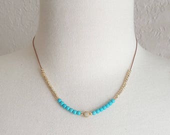 May include: A turquoise and gold beaded necklace with a small, sparkly charm in the center.