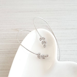 以下が含まれることがあります： 小さな輝く石がついた繊細な葉のデザインのシルバーのバングルブレスレットです。