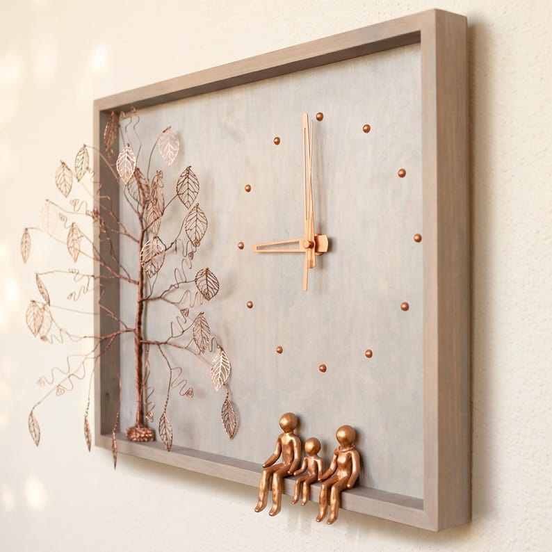 Puede incluir: Un reloj de pared rectangular con marco y esfera de madera gris claro. Presenta manecillas de color cobre, marcadores de hora circulares, un &aacute;rbol tridimensional de alambre de cobre con hojas y tres figuras de color cobre sobre el marco.