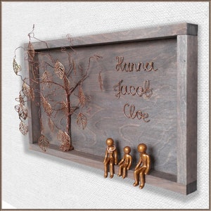 May include: A wooden frame with a wire tree and three small copper figures sitting on a ledge. The names Hanna, Jacob, and Chloe are written in wire on the frame.
