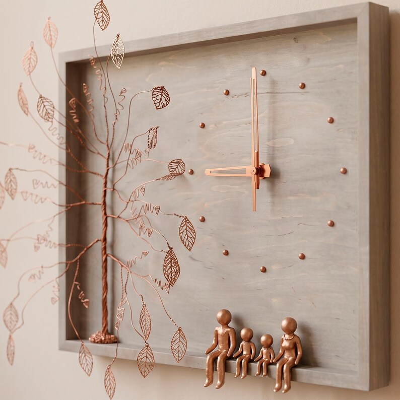 Puede incluir: Un reloj de pared rectangular de madera gris con un &aacute;rbol de alambre color cobre con delicados recortes de hojas en el lado izquierdo. La esfera tiene manecillas y marcadores color cobre, con cuatro figuras color cobre en el marco inferior.