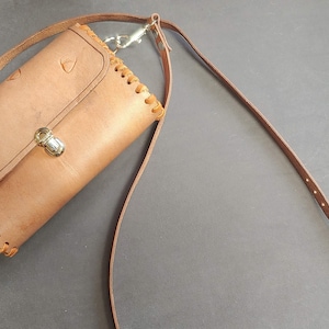 May include: A brown leather crossbody bag with a flap closure and a decorative stitch detail. The bag has a long adjustable strap and a metal clasp.