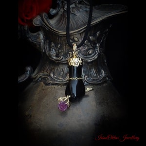 May include: A black onyx pendant necklace with a gold rose and a crown design. The pendant is shaped like a hand holding a rose.