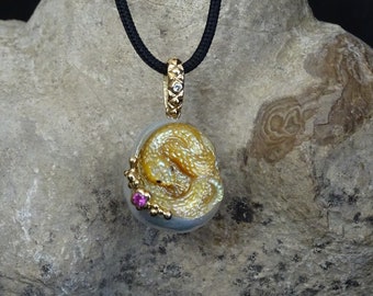 Könnte beinhalten: Goldene Anhänger Halskette mit detailliertem Drachendesign. Der Anhänger hängt an einer schwarzen Kordel und hat eine goldene Öse mit einem kleinen Diamanten. Ein kleiner rosa Edelstein ist auf dem Anhänger gesetzt.