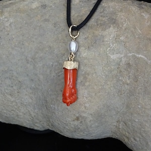 Puede incluir: Un colgante de coral rojo con un engaste de oro y una perla blanca colgando de un cordón negro.