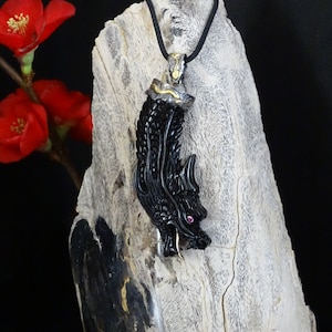 May include: Black dragon pendant necklace with a pink gemstone eye. The pendant is made of carved black stone and has gold accents. The necklace is on a black cord.