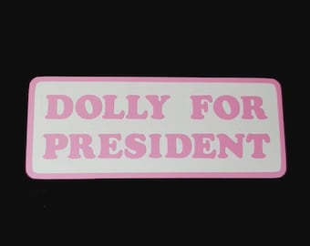 May include: A pink and white sticker with the text "DOLLY FOR PRESIDENT" in a retro font.
