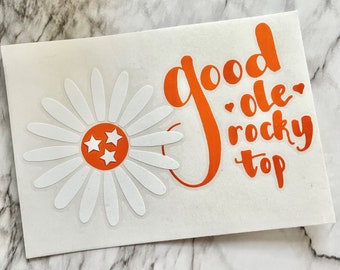 May include: Orange vinyl decal with the text "good ole rocky top" and a white daisy with three orange stars in the centre.