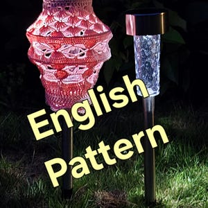 Op de afbeelding: Twee tuinlampen op zonne-energie. Eén heeft een rood en wit gehaakte kap, de andere heeft een heldere, getextureerde glazen buis. De tekst "English Pattern" is zichtbaar.