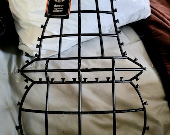 May include: Black metal pumpkin frame for decorating with fall foliage, gourds, or other seasonal items. The frame is shaped like a pumpkin and has a wire mesh design. The tag attached to the frame reads "decor decor".