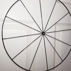 May include: A black metal wreath frame with 12 spokes. The frame is circular and is hanging from a yellow ribbon.