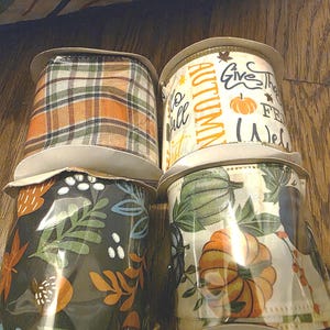 May include: Four spools of decorative ribbon with fall-themed patterns. Designs include plaid, pumpkins, leaves, and the words "Autumn" and "Give Thanks". The ribbons are on cardboard spools.