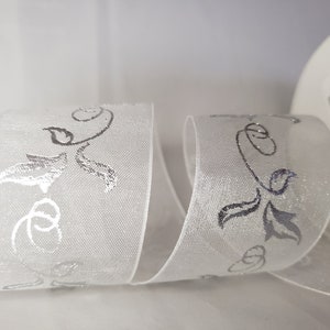 May include: White sheer ribbon with a silver floral design. The ribbon is rolled up on a spool.