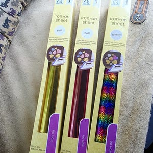 May include: Three packages of iron-on sheets in yellow foil, red foil, and rainbow glitter. Each package is labeled "iron-on sheet" and includes the dimensions 12 in. x 12 in. (30.4 cm x 30.4 cm).