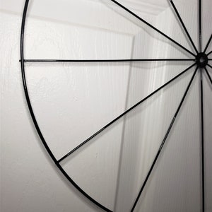 May include: A black metal wreath frame with a circular shape and spokes radiating from the center.