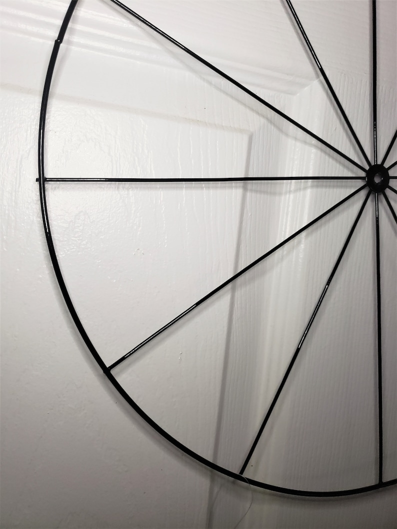 May include: A black metal wreath frame with a circular shape and spokes radiating from the center.