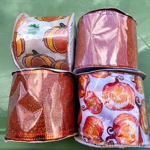 May include: Four rolls of decorative ribbon. Two rolls feature pumpkin patterns, one with orange and brown pumpkins on a white background, and the other with jack-o'-lanterns. The other two rolls are solid orange, one with glitter.