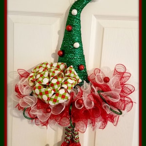 May include: A Christmas wreath shaped like an elf hat with a green and white plaid bow, red and white mesh, and green and red elf shoes.
