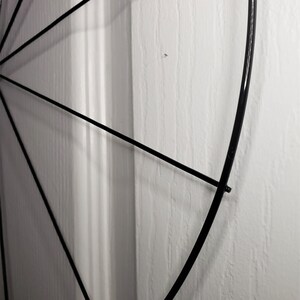 May include: A black metal hoop with spokes radiating out from the center. The hoop is partially obscured by a white wall.