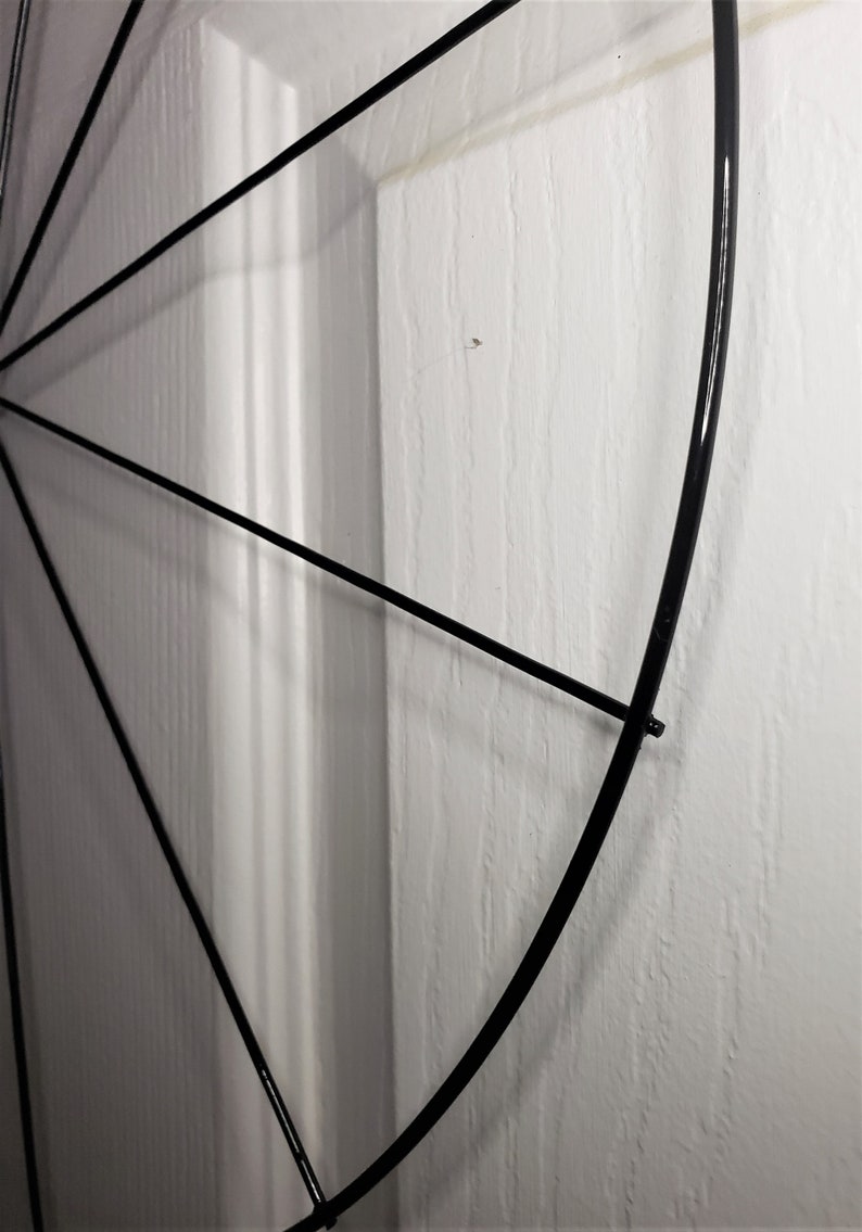 May include: A black metal hoop with spokes radiating out from the center. The hoop is partially obscured by a white wall.