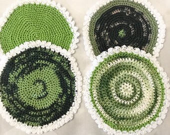 May include: Four crocheted coasters in shades of green with white crochet edging. The coasters have a circular shape and a spiral pattern.