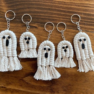 May include: Five white crocheted ghost keychains with black felt eyes and mouths. The keychains are hanging from silver key rings.
