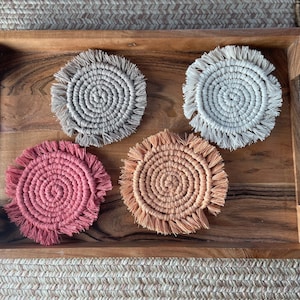 May include: Four round crocheted coasters with fringe. Two are beige, one is peach, and one is pink.