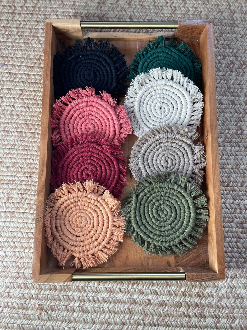 May include: A set of eight round crocheted coasters in a wooden tray. The coasters are in various colors, including black, green, cream, pink, red, and peach.