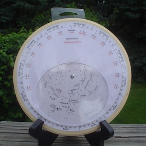 May include: A white circular star chart with a black stand. The chart shows the constellations visible in the Northern Hemisphere. The chart is labeled with the months of the year and the times of day. The text "Standard Time" and "Daylight Saving Time" is printed on the chart.