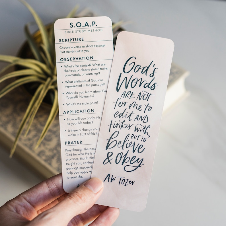 May include: A pink and white bookmark with a quote from A.W. Tozer that reads "God's Words Are Not For Me To Edit And Tinker With, But To Believe & Obey."