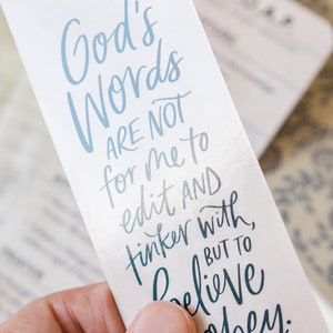 May include: A white bookmark with blue lettering that reads "God's Words Are Not For Me To Edit And Tinker With, But To Believe."