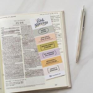 May include: A colorful bookmark with the title "Bible Markings" and different sections for names of God, who God is and what He does, repeated words and phrases, sin, warnings, and evil enemies, application/what's for me, and similes and metaphors. The bookmark is on a page of a Bible.