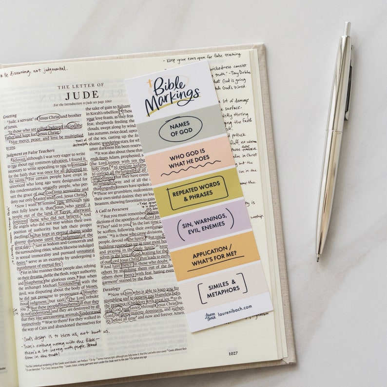 May include: A colorful bookmark with the title "Bible Markings" and different sections for names of God, who God is and what He does, repeated words and phrases, sin, warnings, and evil enemies, application/what's for me, and similes and metaphors. The bookmark is on a page of a Bible.