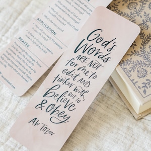 May include: A pink bookmark with a quote in black script that reads "God's Words Are Not For Me To Edit And Tinker With, But To Believe & Obey." The quote is attributed to A.W. Tozer.