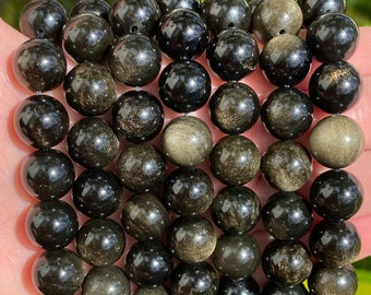 May include: A strand of black and gold gemstone beads. The beads are round and have a smooth, polished finish. The beads are strung on a clear elastic cord.