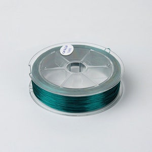 May include: A spool of teal green thread wound around a clear plastic bobbin. The bobbin has a label that reads "44443 40001".
