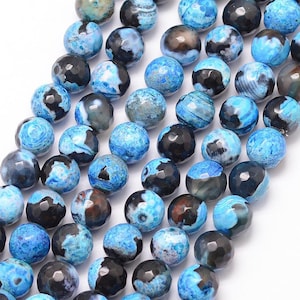 Puede incluir: Una hebra de cuentas de ágata azul con patrones negros y blancos. Las cuentas son facetadas y tienen un aspecto natural y orgánico.
