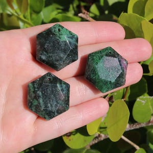 May include: Three green and black gemstone pendants in the shape of a six-pointed star. The pendants have a hole at the top for stringing.