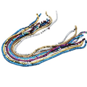 May include: A strand of iridescent square beads in various colors, including blue, gold, silver, and purple. The beads are strung together to form a long necklace.