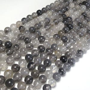 May include: A strand of round, gray and clear smoky quartz beads. The beads are smooth and polished, with a slight variation in color and translucency.