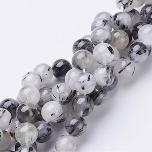 May include: A strand of round, translucent, white beads with black inclusions. The beads are approximately 8mm in diameter.