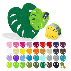 Könnte beinhalten: Set mit 36 Filz-Untersetzern in Monstera-Blattform in verschiedenen Farben, darunter Pink, Rot, Orange, Gelb, Grün, Blau, Lila und Braun. Die Untersetzer sind herzförmig und haben ein ausgeschnittenes Design, das einem Monstera-Blatt ähnelt. Das Wort "FILZ" ist auf einem der Untersetzer aufgedruckt.