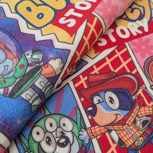 May include: A colorful fabric featuring comic book style panels with cartoon characters. The panels include the text "BLUE STORY" and images of a space ranger, a three-eyed alien, and a dog dressed as a cowboy.